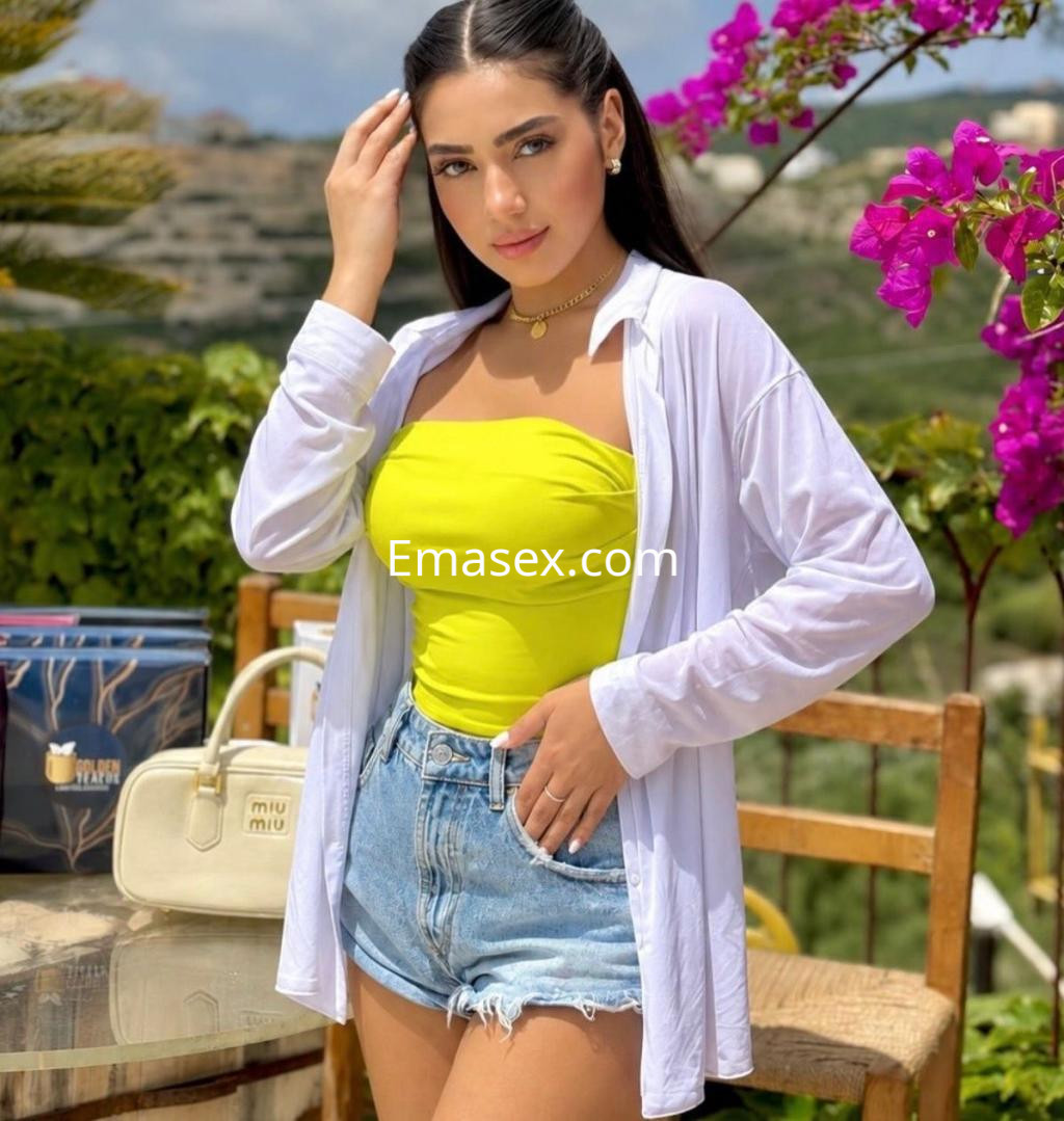 Puta con blusa blanca y top amarillo, sentada en una terraza de Bilbao con flores rosas de fondo.