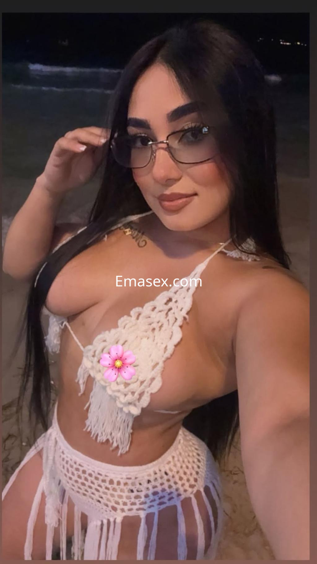 Puta en Sevilla se toma una selfie en la playa, luciendo un bikini blanco y gafas de sol, con cabello largo y lacio.
