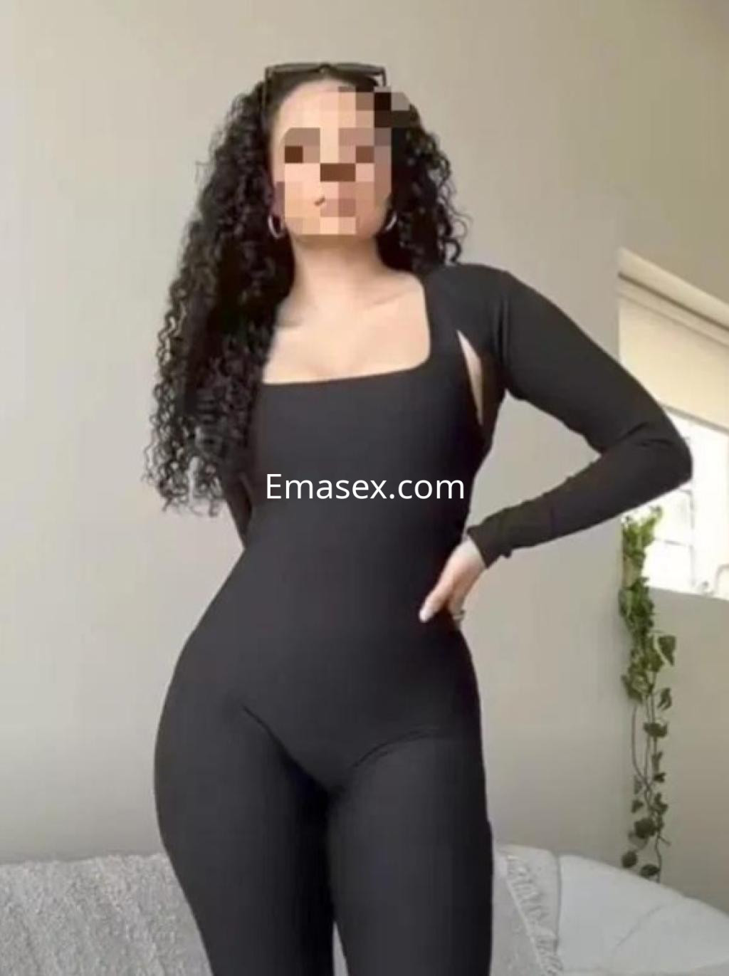 Escort en Vigo luciendo un ajustado mono negro de manga larga, con cabello rizado y un entorno minimalista.
