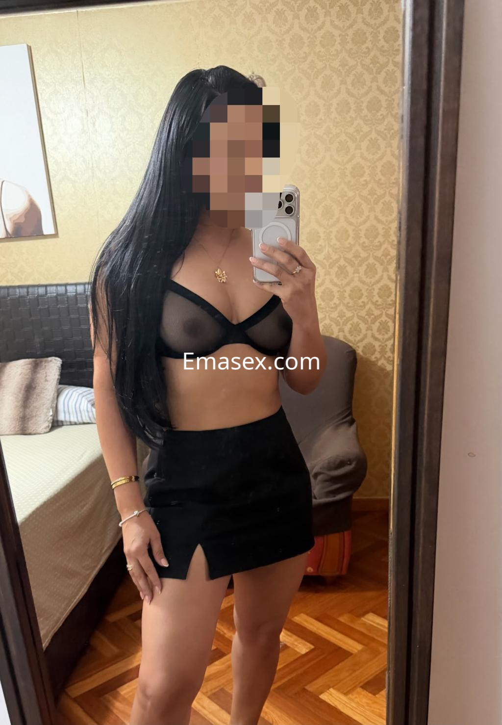 Escort en Santiago, posando frente a un espejo con un top negro transparente y una falda corta ajustada.