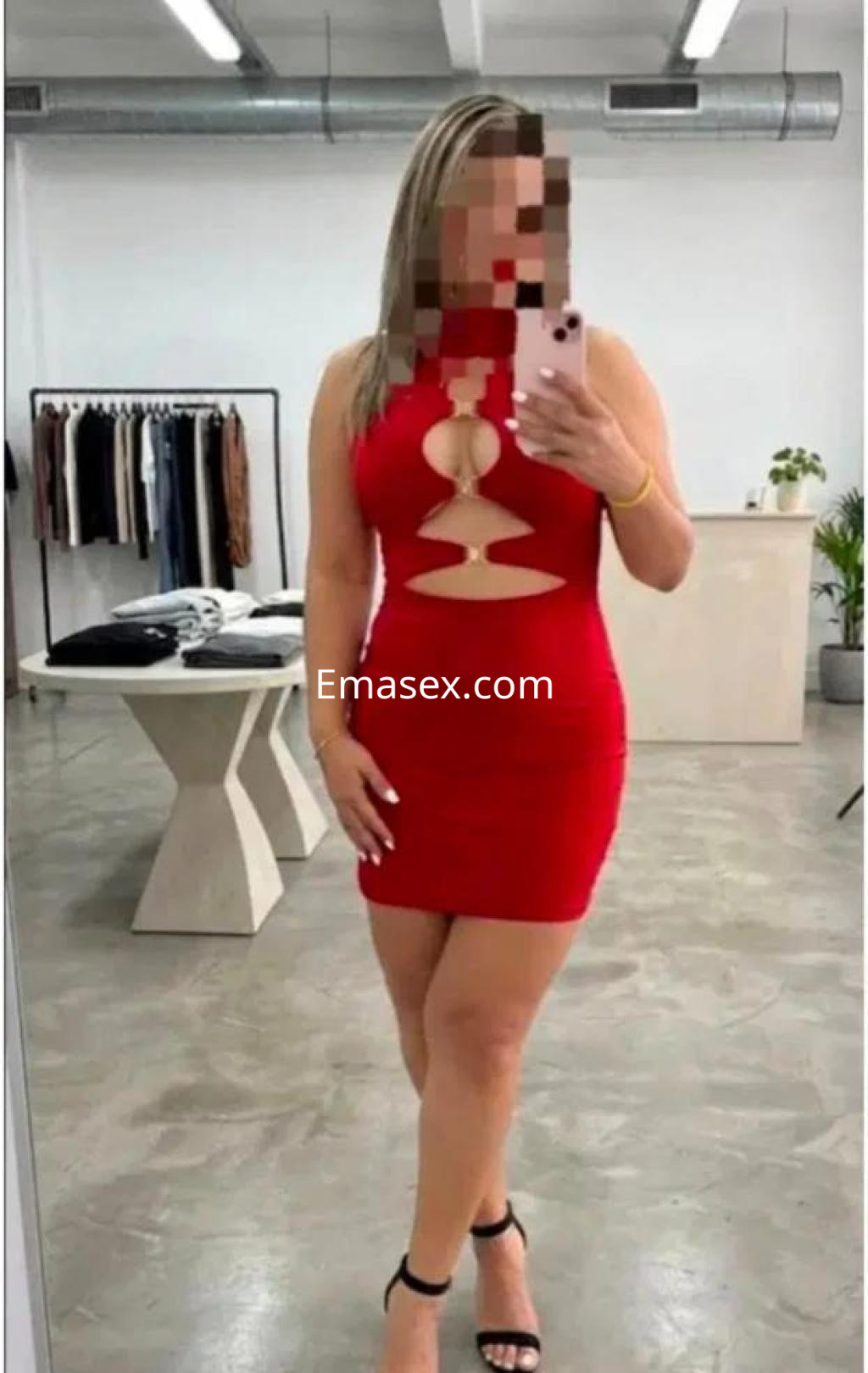 Puta en Albacete viste un vestido rojo ajustado con cortes en el torso, posando frente a un espejo.