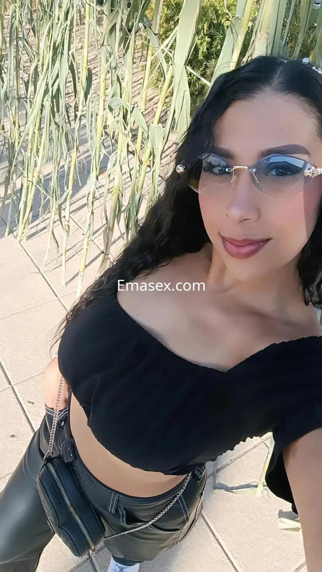 Escort en Palma de Mallorca con blusa negra ajustada y pantalones de cuero, posando con gafas de sol.
