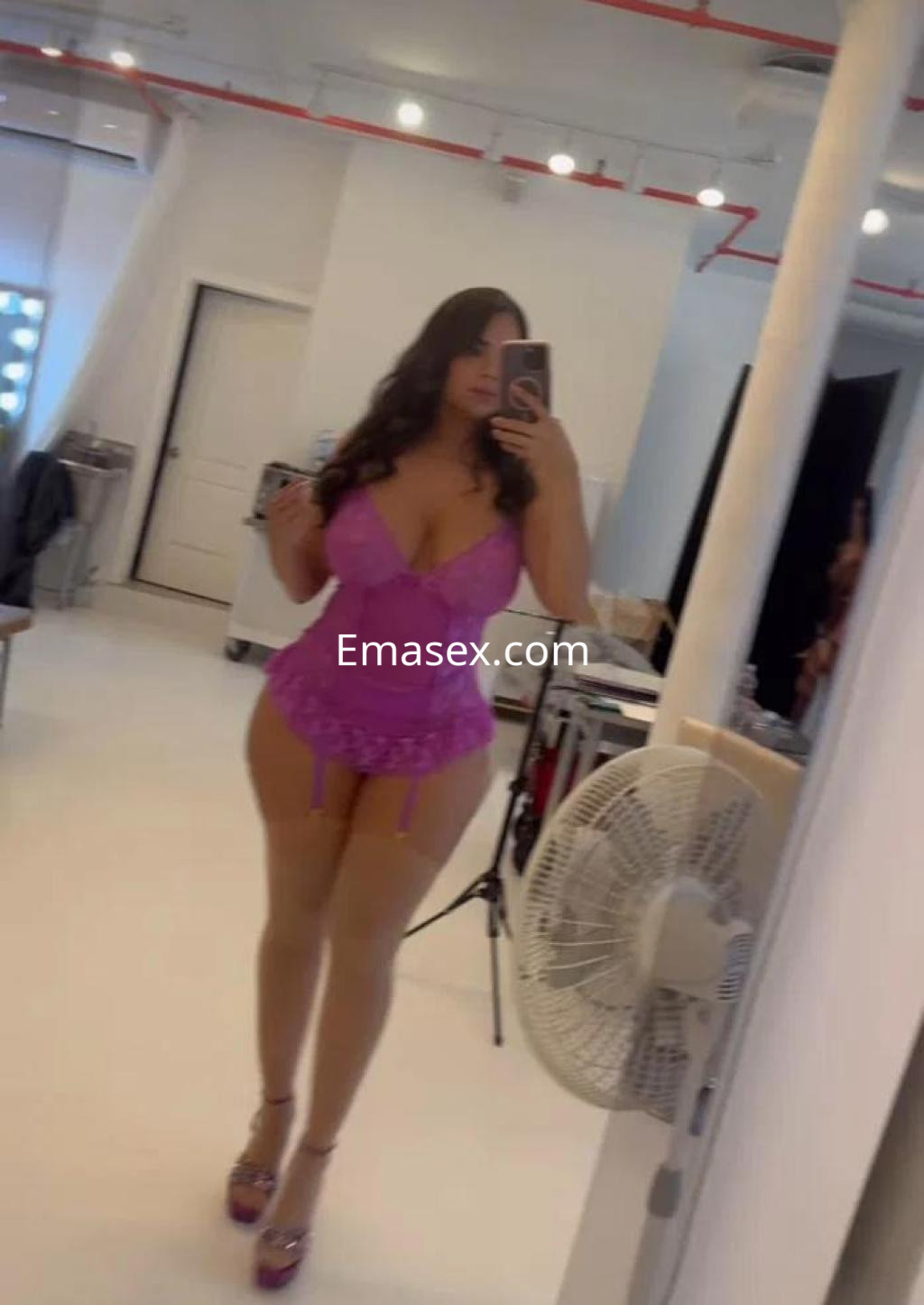 Escort en Barcelona posando frente a un espejo, viste un conjunto de lencería rosa y tacones altos.