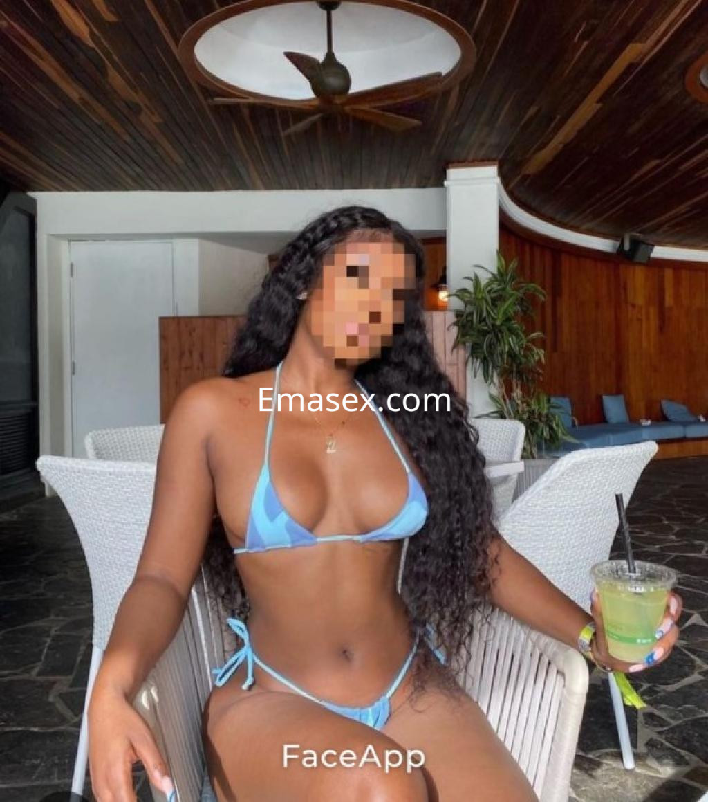 Escort en Burgos con cabello largo y rizado, vistiendo un bikini azul, posando en un ambiente tropical.