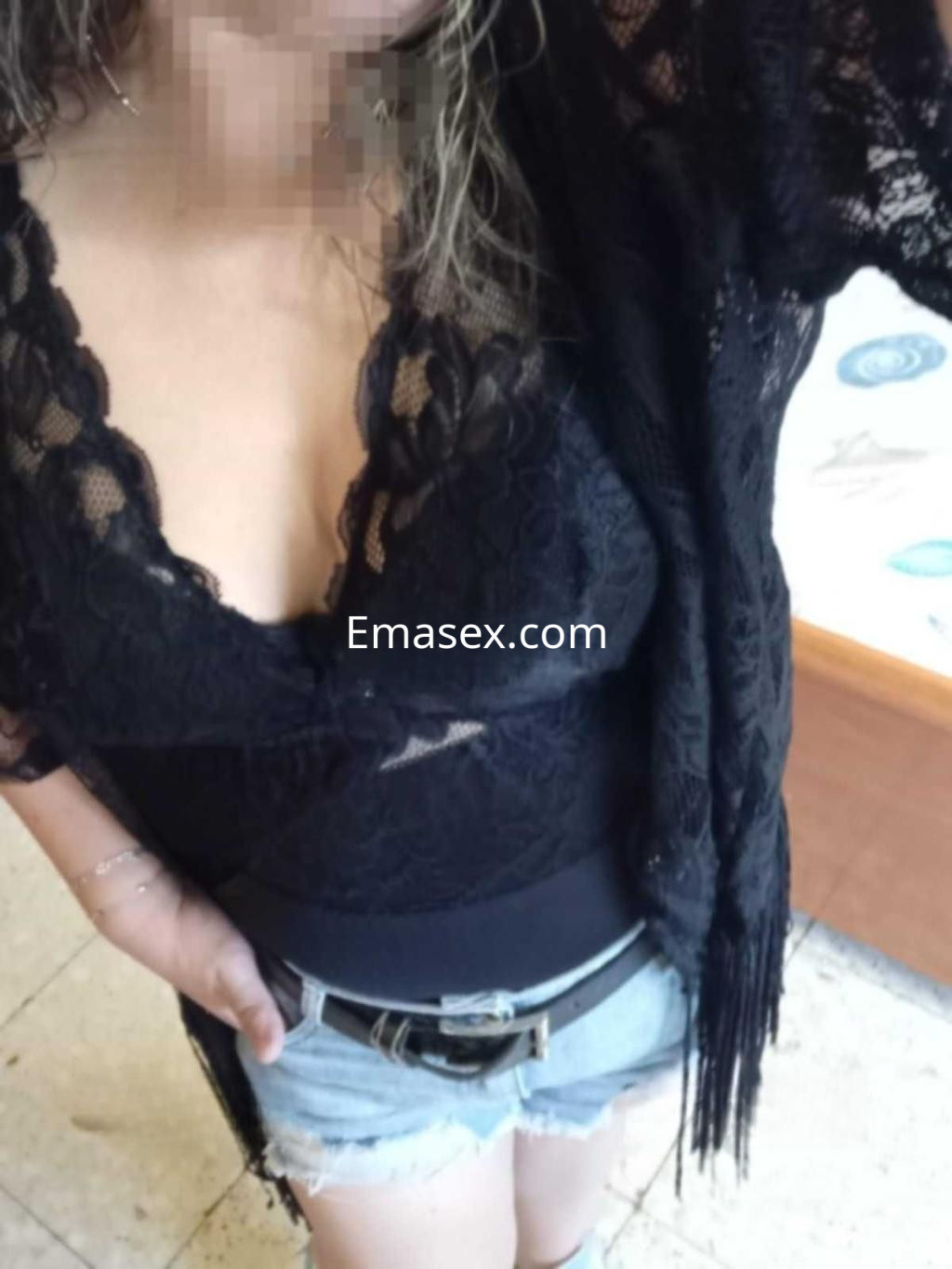 Puta en Córdoba luciendo un top de encaje negro y shorts de mezclilla, con cabello rizado y suelto.