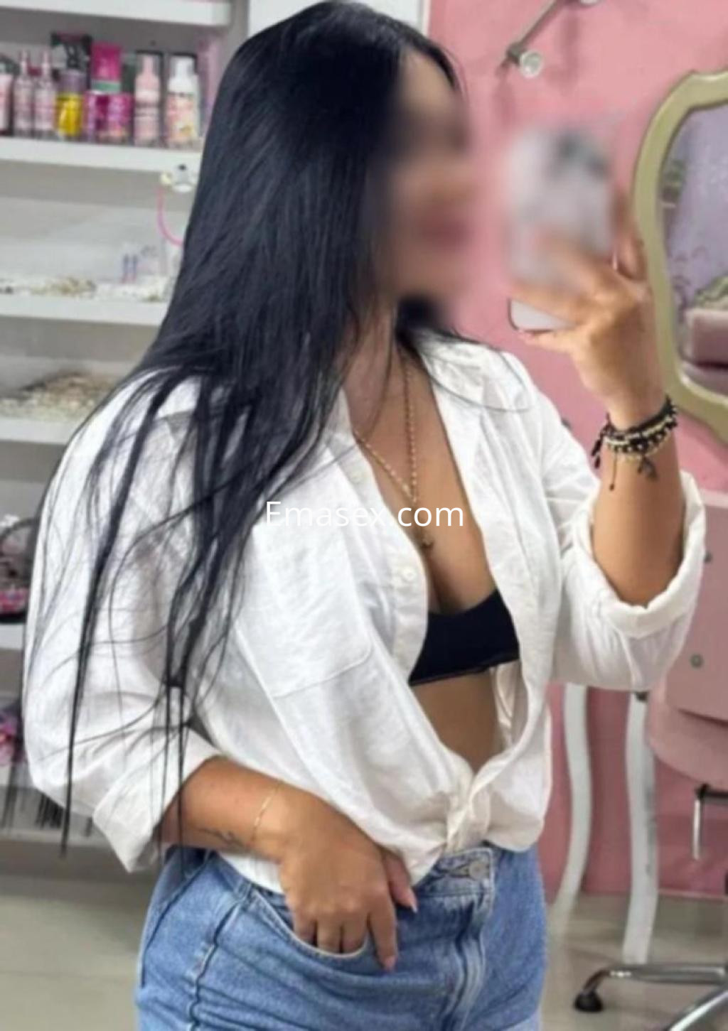Escort en Córdoba posando con una camisa blanca abierta sobre un top negro y jeans ajustados, mostrando su largo cabello oscuro.