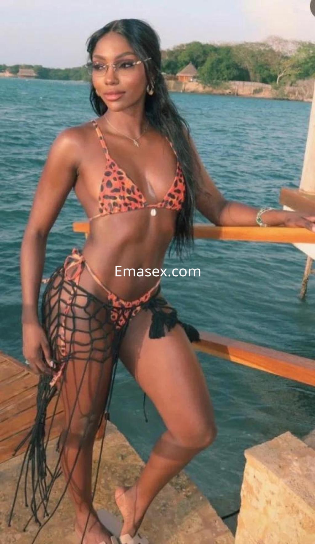 Escort en Lleida luciendo un bikini de leopardo y una falda de red, posando junto al agua.