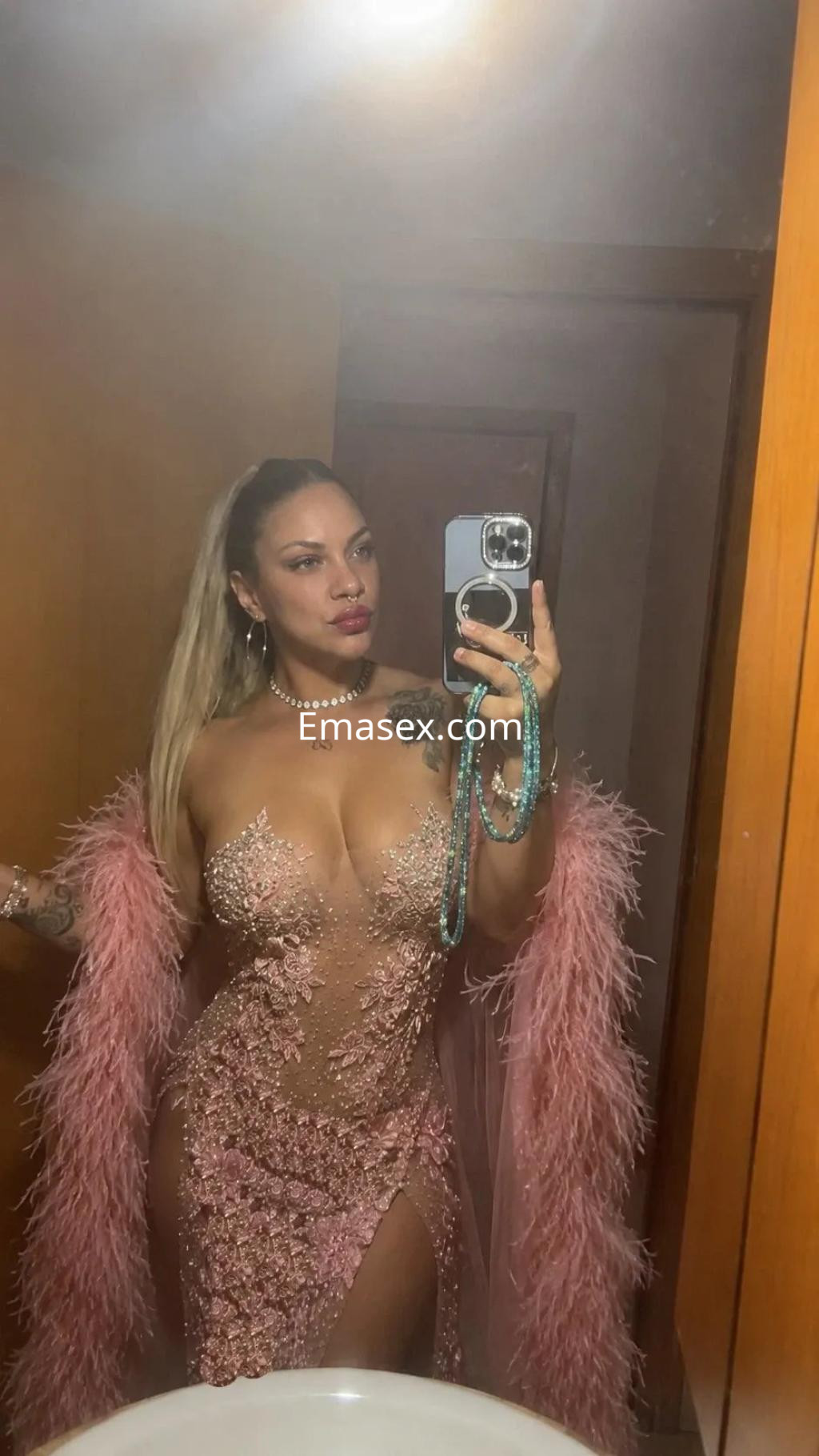 Escort en Murcia con vestido ajustado rosa claro y detalles brillantes, posando frente al espejo.