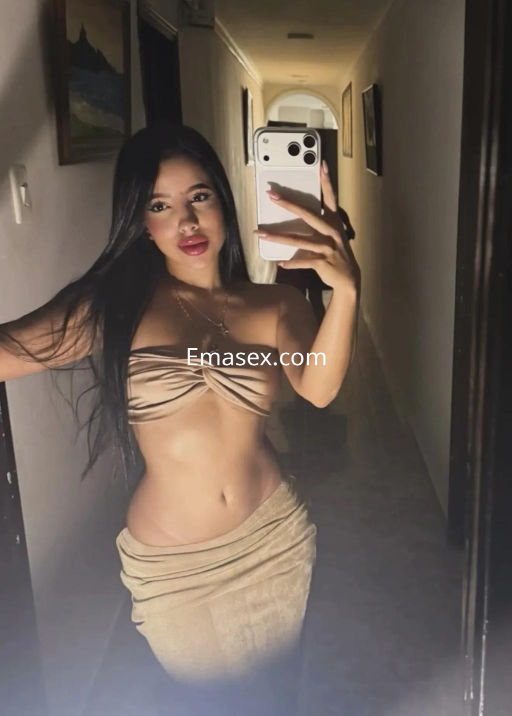 Puta en Toledo se toma una selfie en un pasillo, luciendo un top beige y una falda ajustada, con cabello largo.
