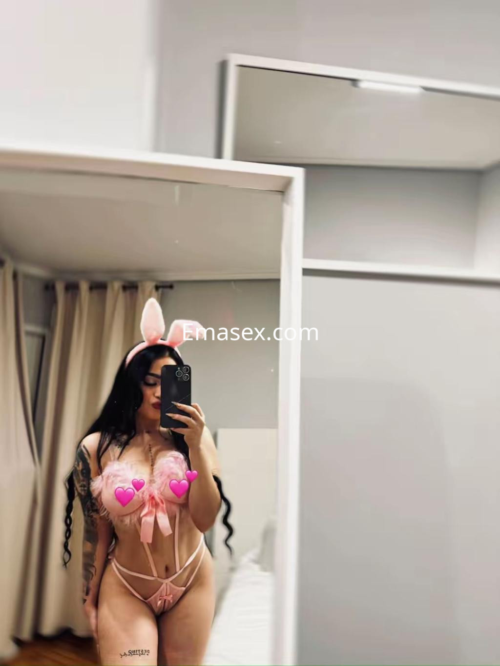 Escort en Vigo con orejas de conejo y lencería rosa transparente, posando frente a un espejo.