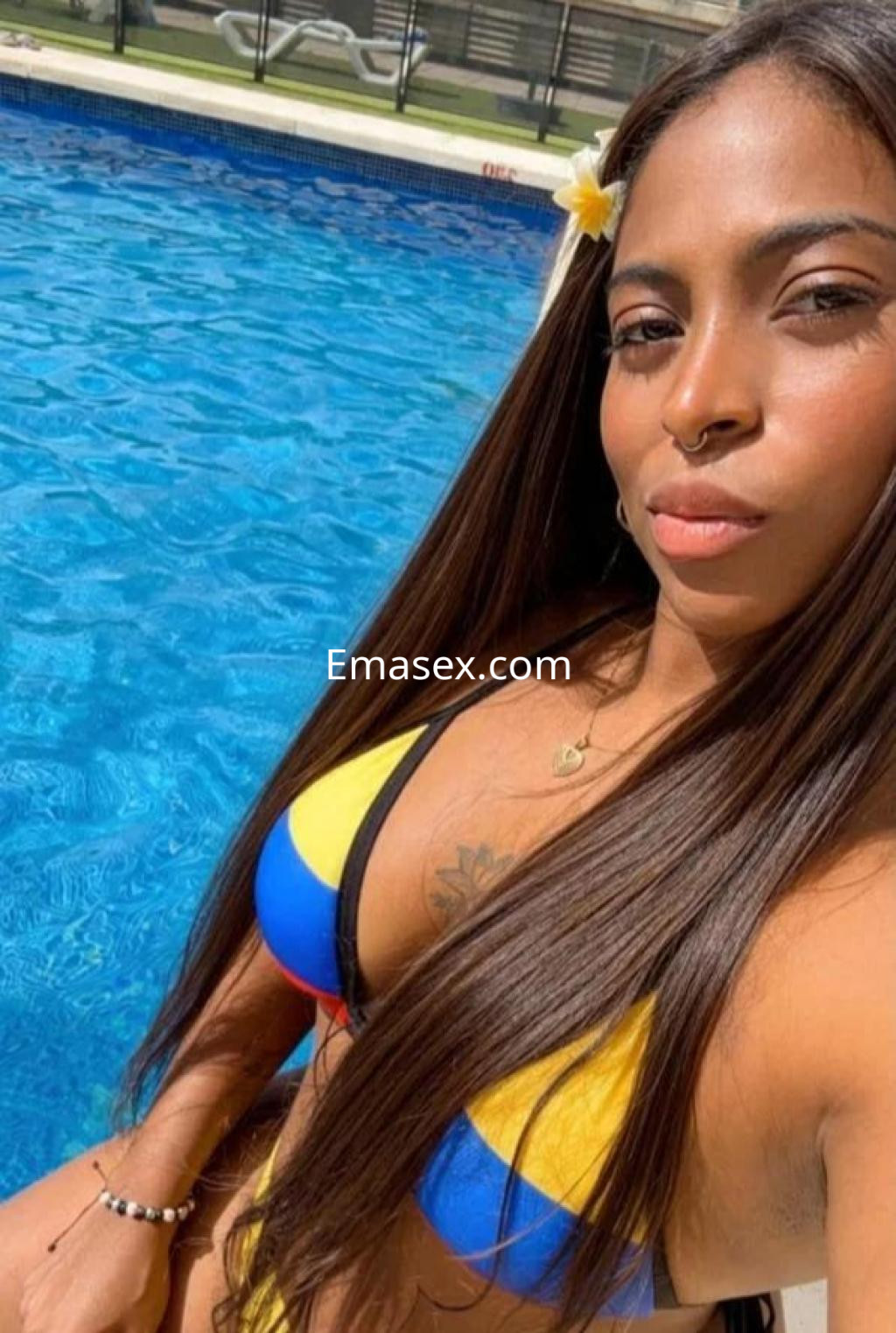 Puta con cabello largo y lacio, luciendo un bikini amarillo y azul junto a una piscina en Sevilla.