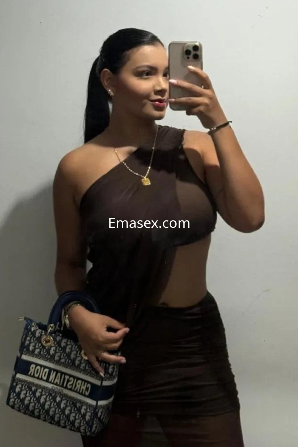 La escort en Málaga posa para un selfie, vistiendo una blusa asimétrica y llevando un bolso de diseño.