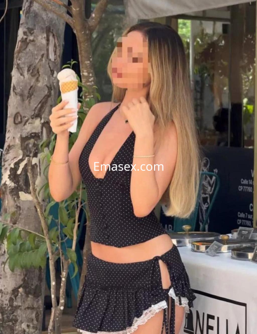 La puta en Cádiz luce un top negro con lunares y una falda corta mientras sostiene un helado.