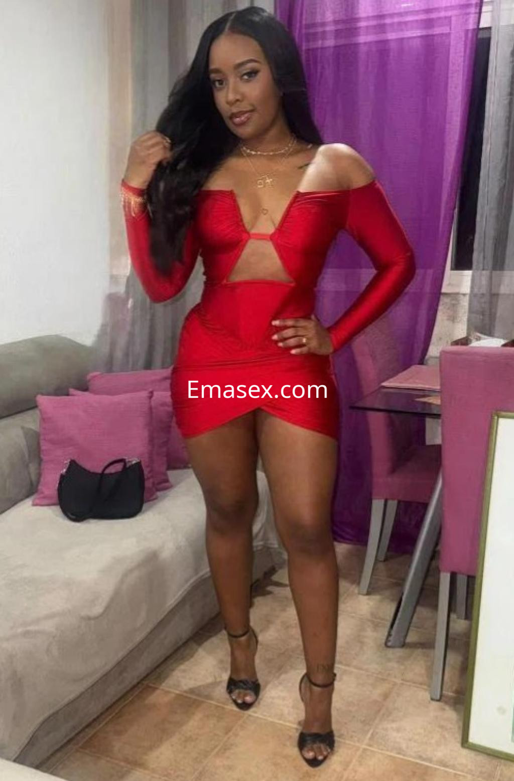 Escort en Castellón viste un ceñido vestido rojo con escote, posando con confianza en un ambiente moderno.
