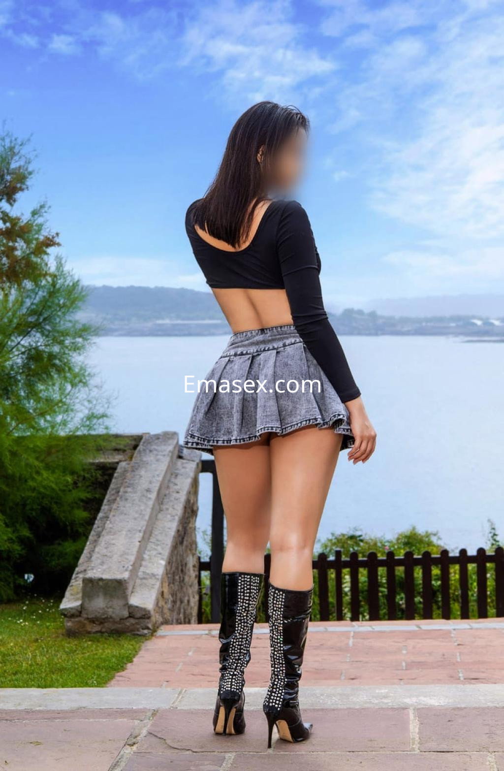 Puta en Bilbao lleva un top negro de espalda descubierta y una falda corta de mezclilla, posando junto al agua.