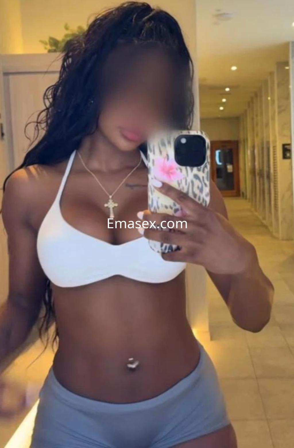 Puta posando en un espejo con bikini blanco y pantalones cortos grises, en un entorno moderno en Huelva.