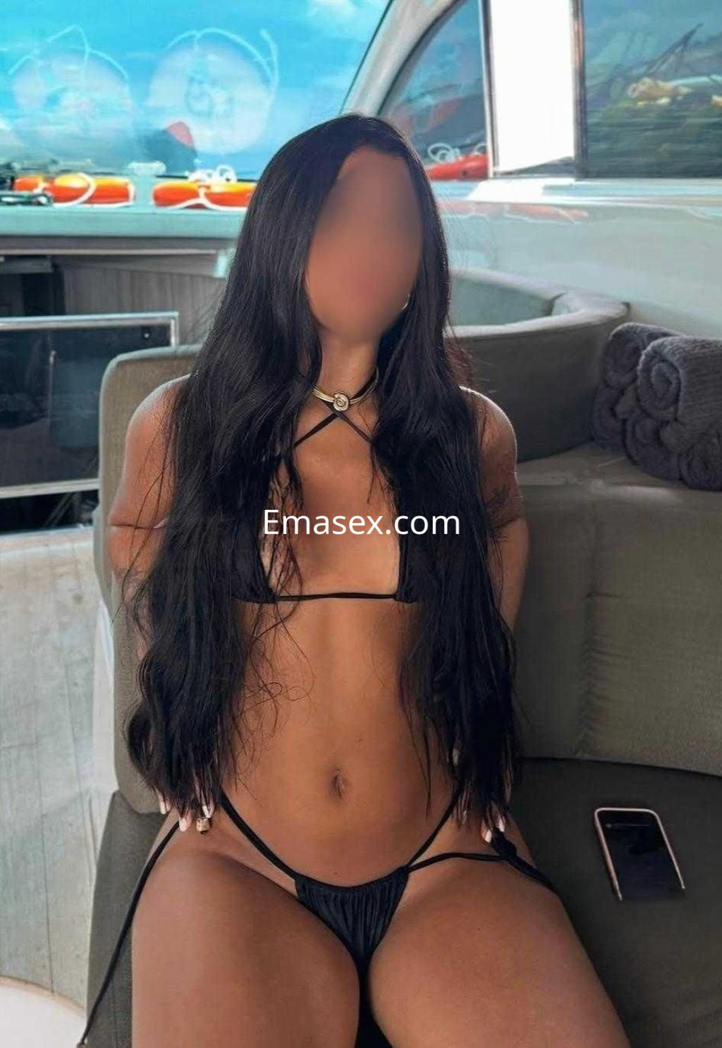 Puta en Huelva sentada en un yate, vistiendo un bikini negro y con cabello largo y lacio.