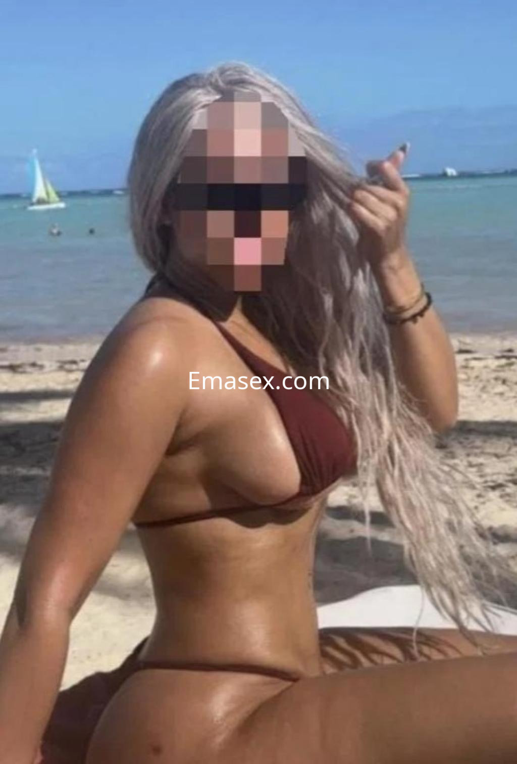 Escort de cabello largo y platinado, con bikini marrón, posando en la playa de Cádiz bajo el sol.