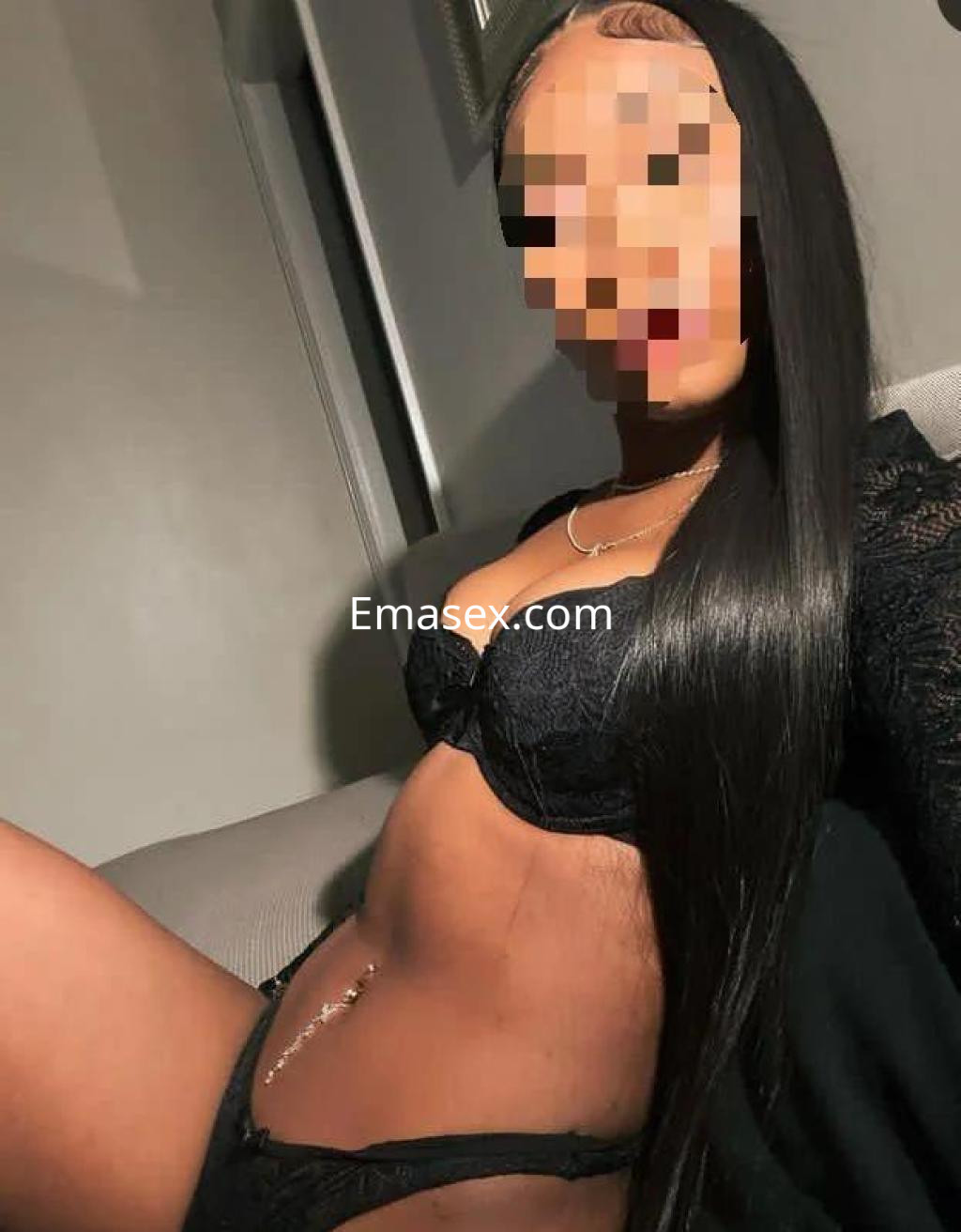 Escort en Lleida con cabello largo y lacio, vistiendo lencería negra, posando de lado en un ambiente interior.