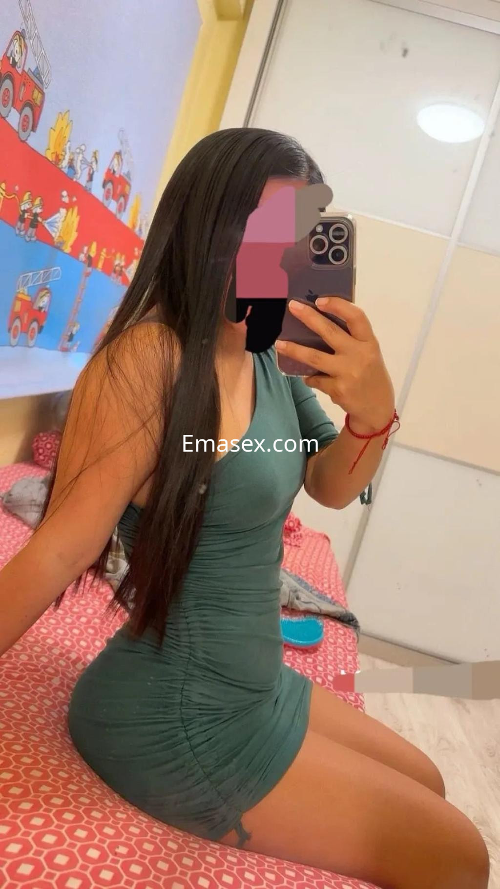 Puta en Valencia con vestido verde ajustado, posando de perfil frente a un espejo en una habitación decorada.