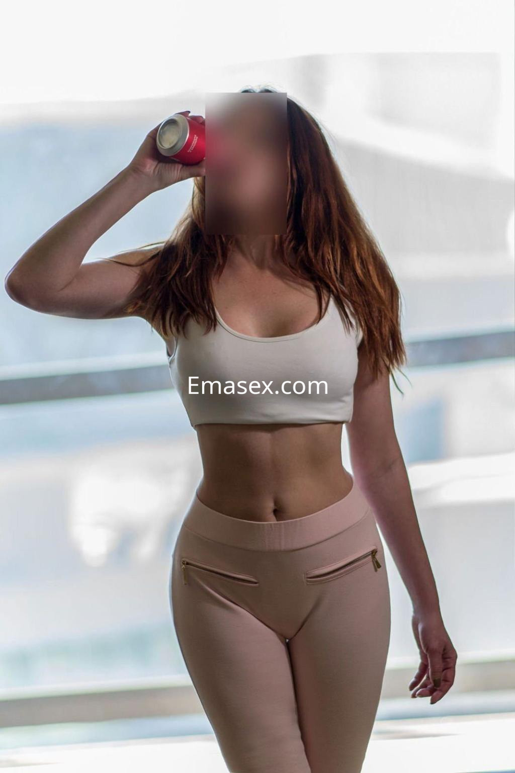 Escort en Valencia con cabello largo y castaño, viste top blanco y leggins rosa, sosteniendo una bebida.