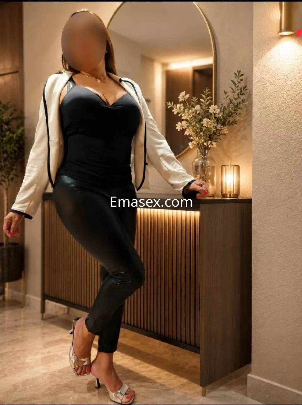 Puta en Valencia, luciendo una blusa negra ajustada y pantalones de cuero, posando en un ambiente elegante.