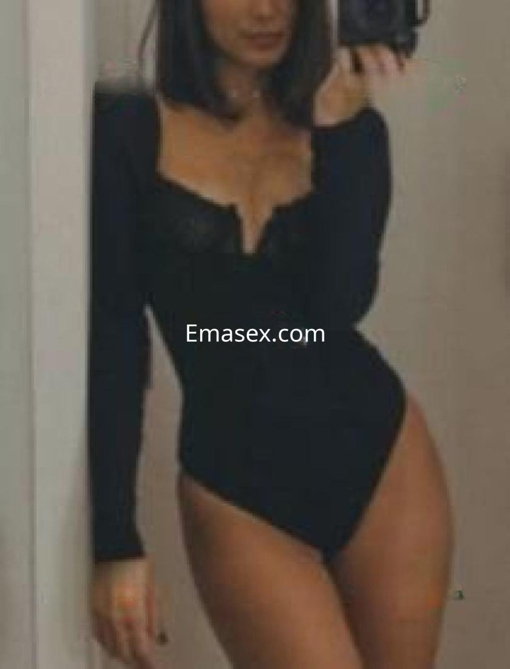 Escort en Zaragoza posando frente al espejo con un body negro de manga larga y detalles de encaje.