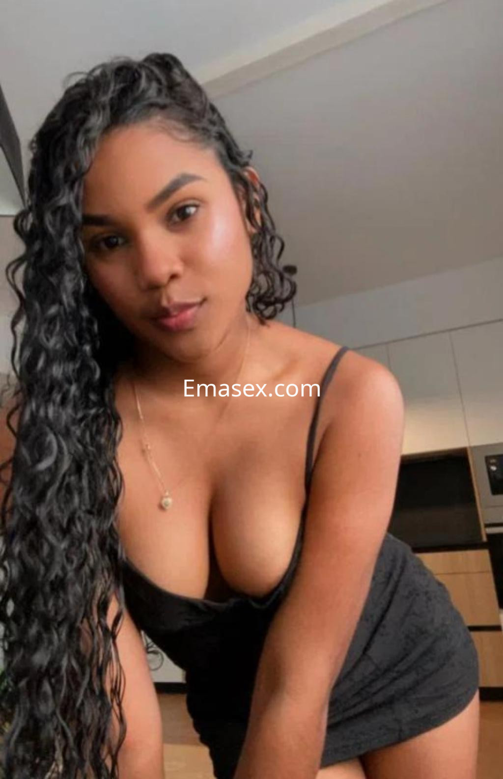 Escort en Sevilla con cabello rizado y largo, vistiendo un vestido negro ajustado en un ambiente moderno.