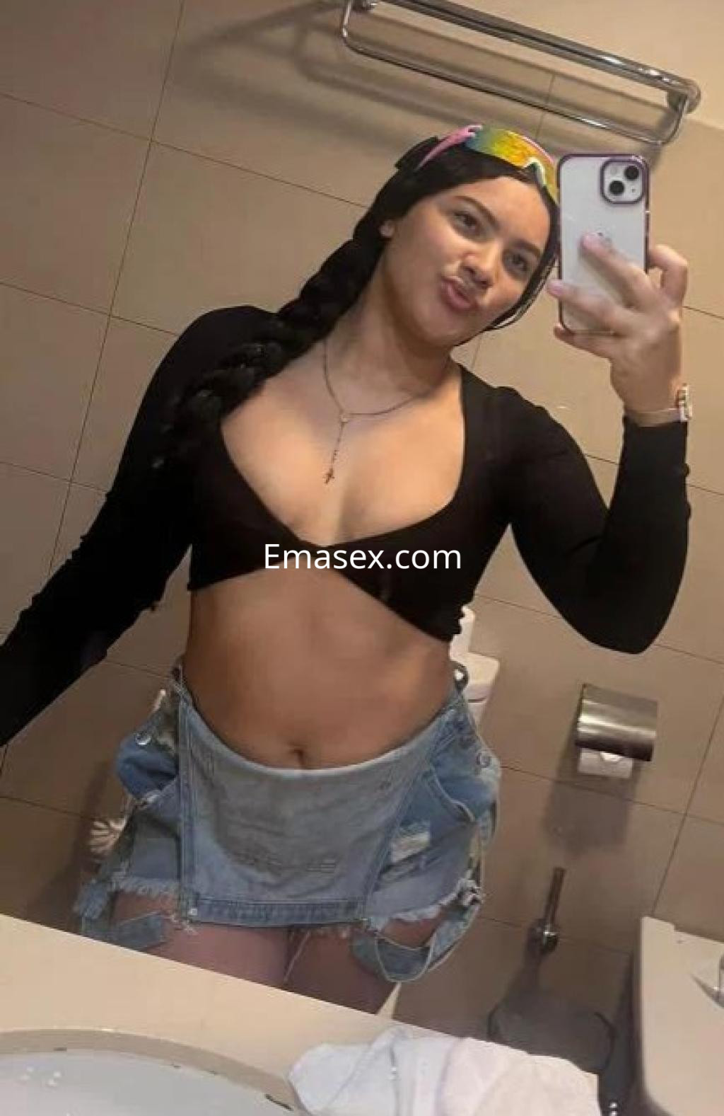 Escort en Cádiz, posando frente al espejo con un top negro y una falda de mezclilla, mostrando confianza.