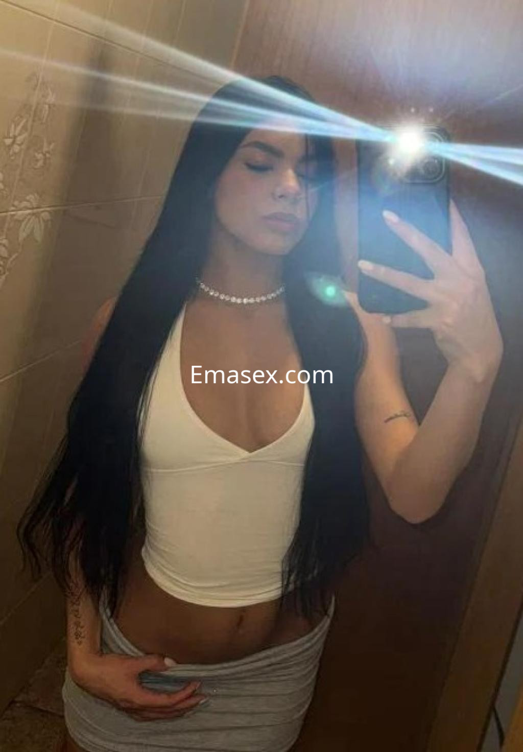 Escort en Granada con cabello largo y oscuro, luciendo una blusa blanca y una falda corta mientras se toma un selfie.