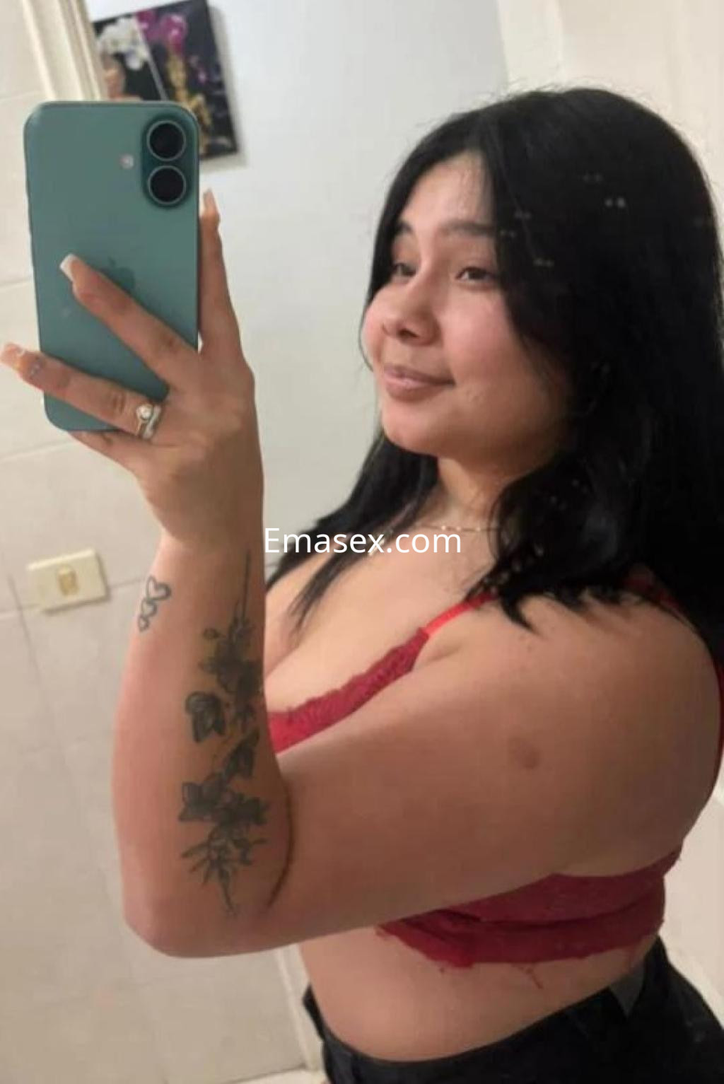Escort en Tenerife con cabello oscuro y lacio, vistiendo un top rojo y pantalones oscuros, posando en un espejo.