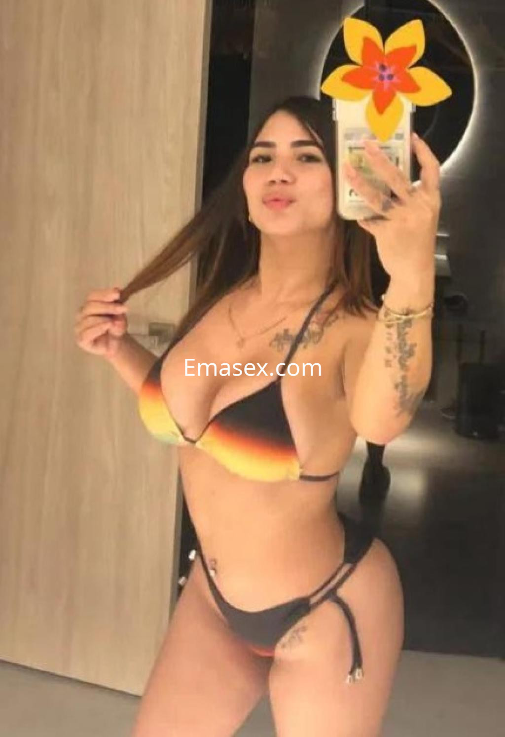 Puta posando en un espejo con un bikini en tonos negro y naranja, mostrando su figura y cabello largo.