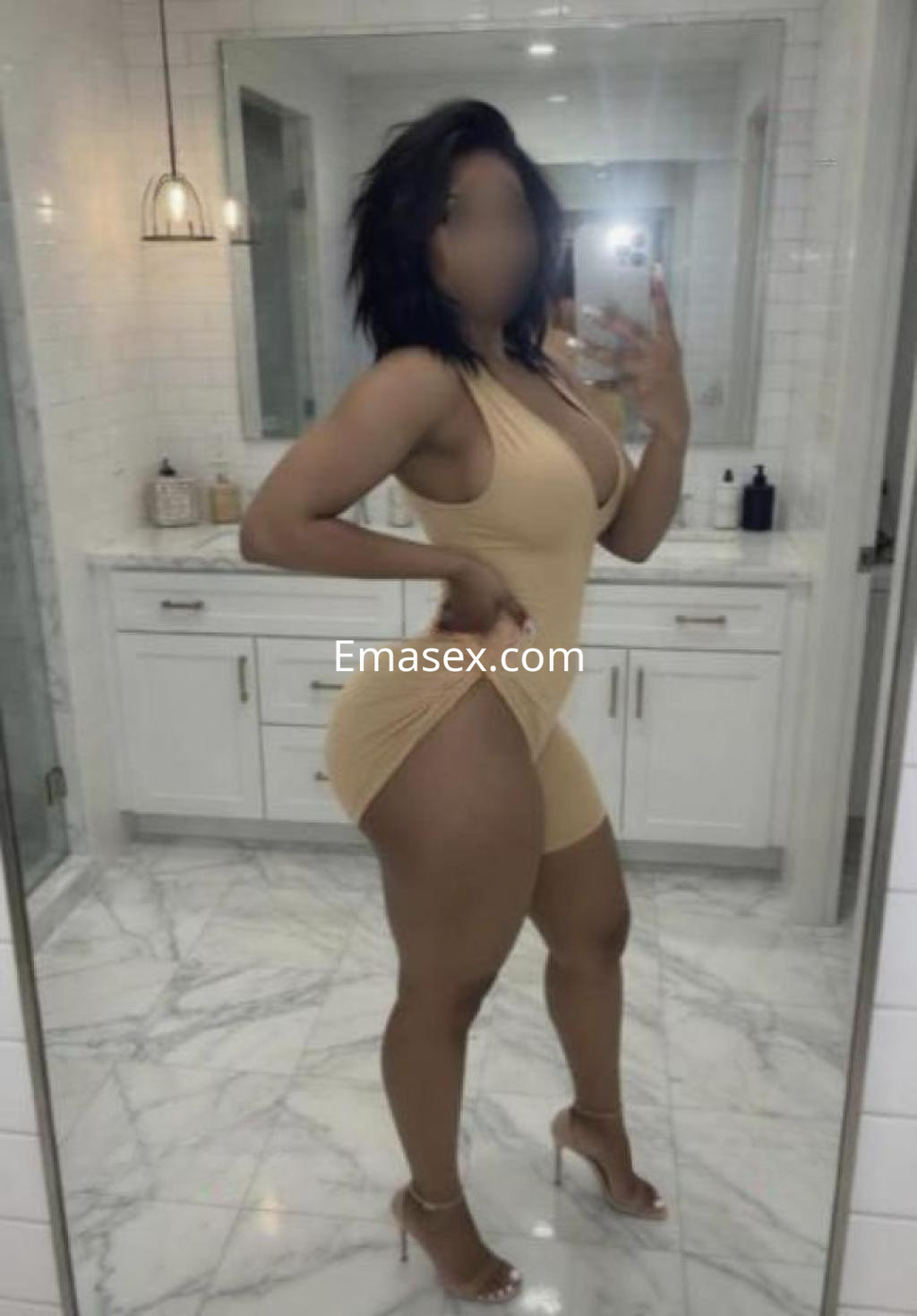 Escort en Albacete mostrando su silueta en un vestido ajustado color nude, con tacones altos en un baño moderno.