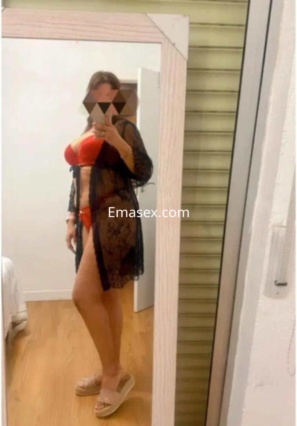 Escort en Almería posando en un espejo, vistiendo un bikini rojo y una bata negra, con sandalias claras.