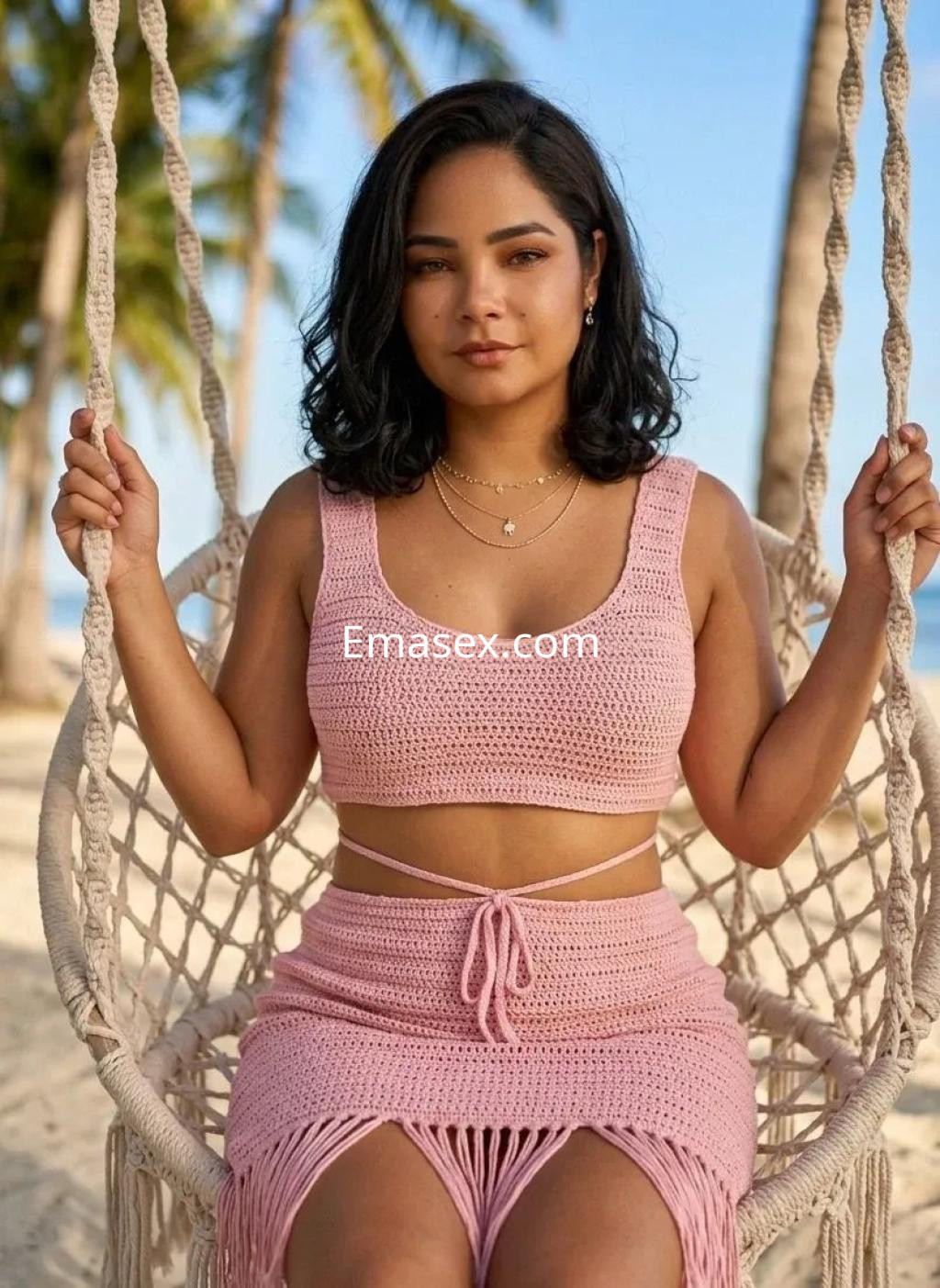 Escort en Palma de Mallorca sentada en una hamaca, vistiendo un conjunto de crochet rosa y con cabello oscuro.