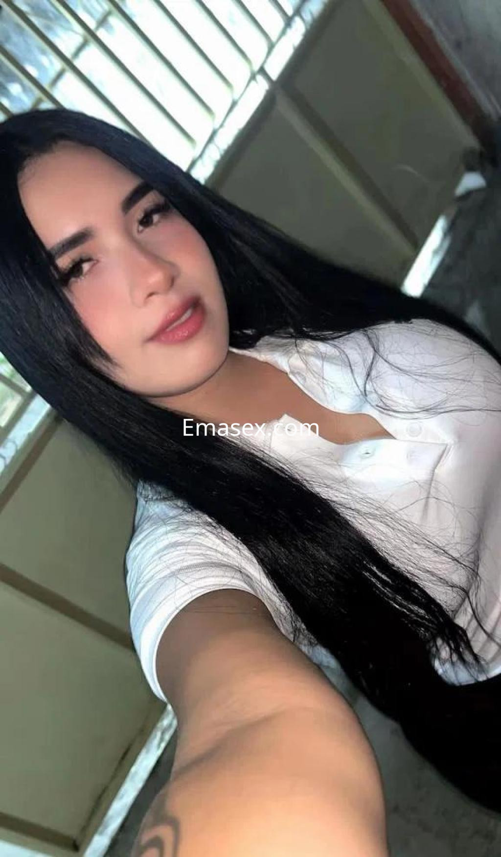 Puta con cabello largo y oscuro, vistiendo una camiseta blanca, posando en un entorno interior en Barcelona.