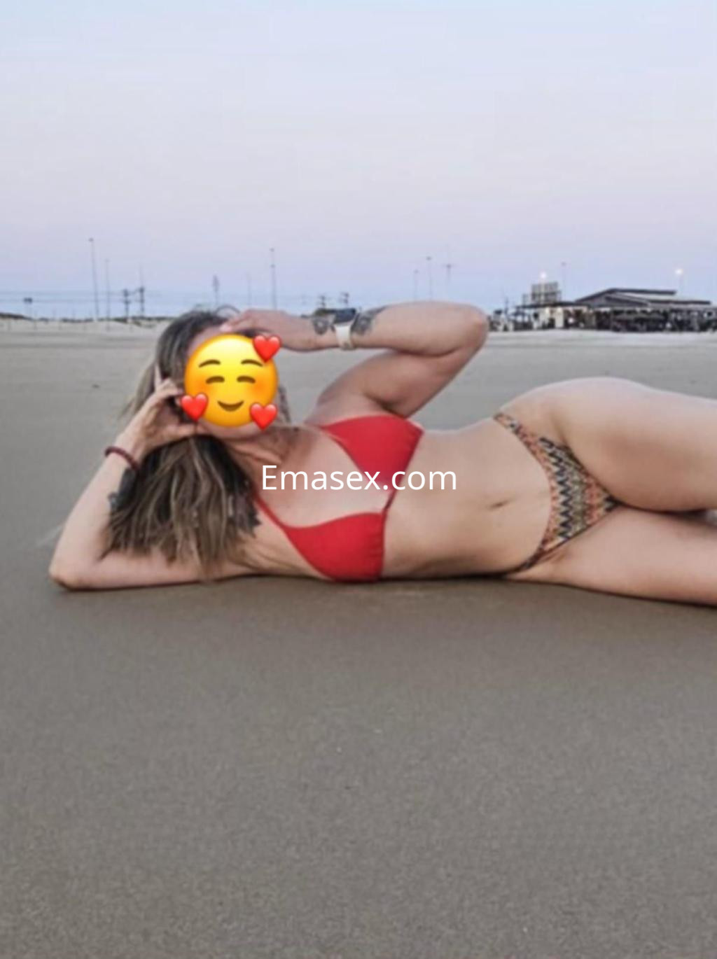 Puta en Cádiz recostada sobre la arena, viste un bikini rojo y tiene cabello castaño claro.