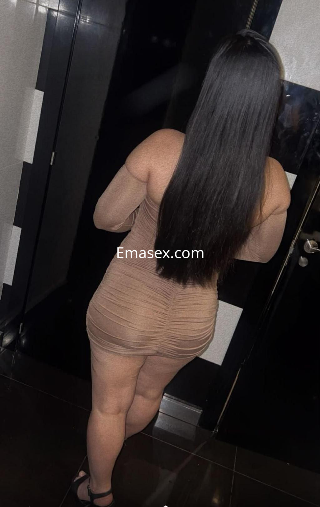 Puta con vestido ajustado color nude que resalta sus curvas, de espaldas en un ambiente elegante en Castellón.