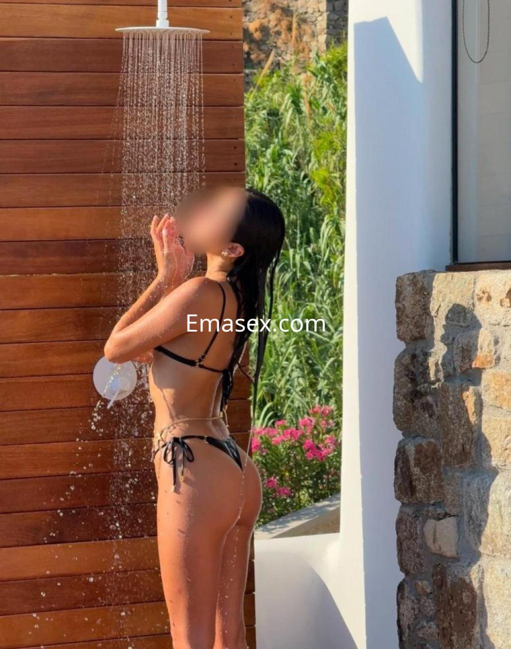 Escort en Lleida luciendo un bikini negro mientras se ducha al aire libre, con una postura relajada.