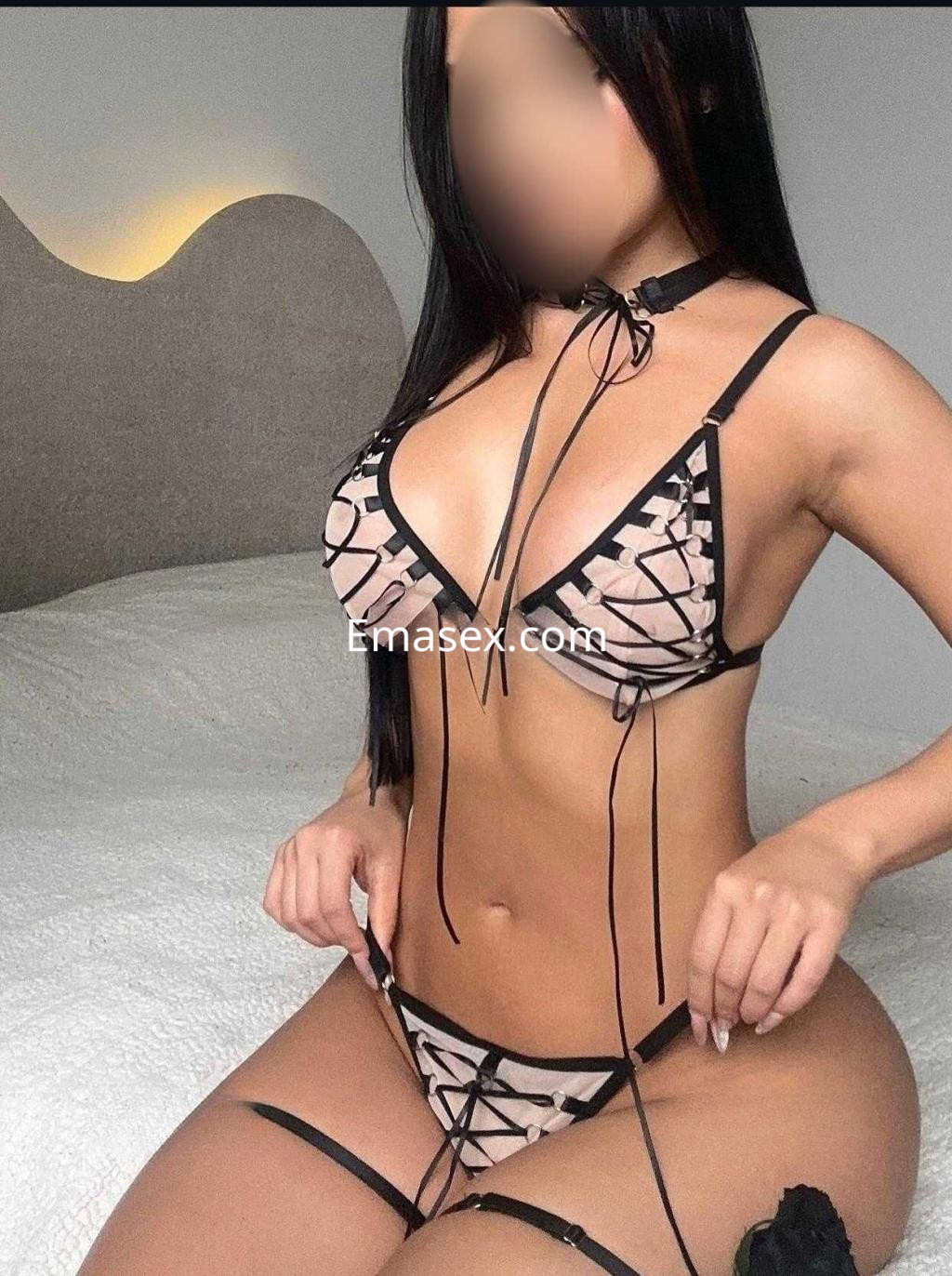Puta posando en la cama con un conjunto de lencería transparente en tonos nude y negro en Tenerife.