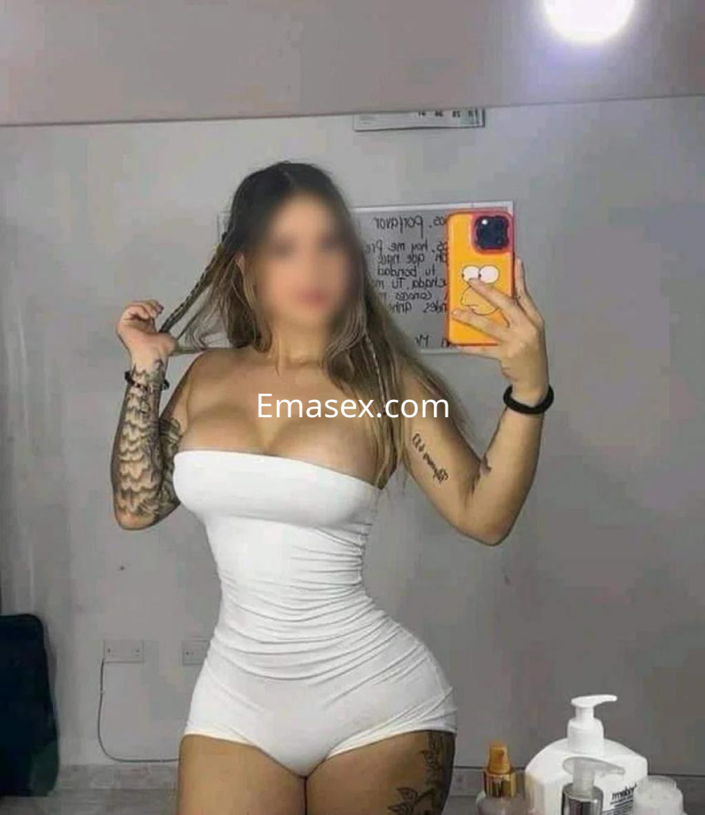 Escort en Tarragona con cabello largo y lacio, luciendo un ajustado mono blanco y mostrando un tatuaje en el brazo.