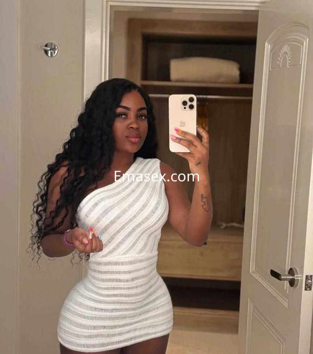 La puta en Toledo posa con un vestido blanco de un hombro mientras se toma una selfie en un espejo.