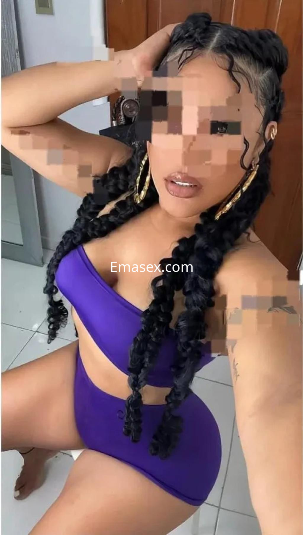 Puta en Valladolid luce un bikini morado, con cabello trenzado y grandes aretes, posando de manera seductora.