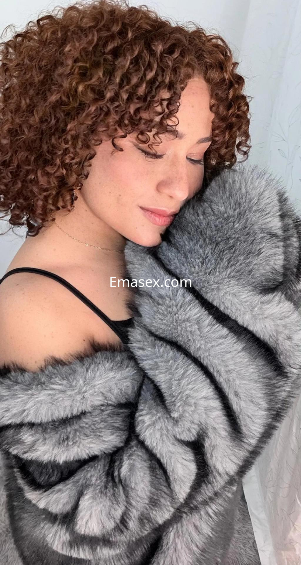 Escort en Valladolid con cabello rizado castaño claro, vistiendo una chaqueta de piel sintética gris y con una pose suave.