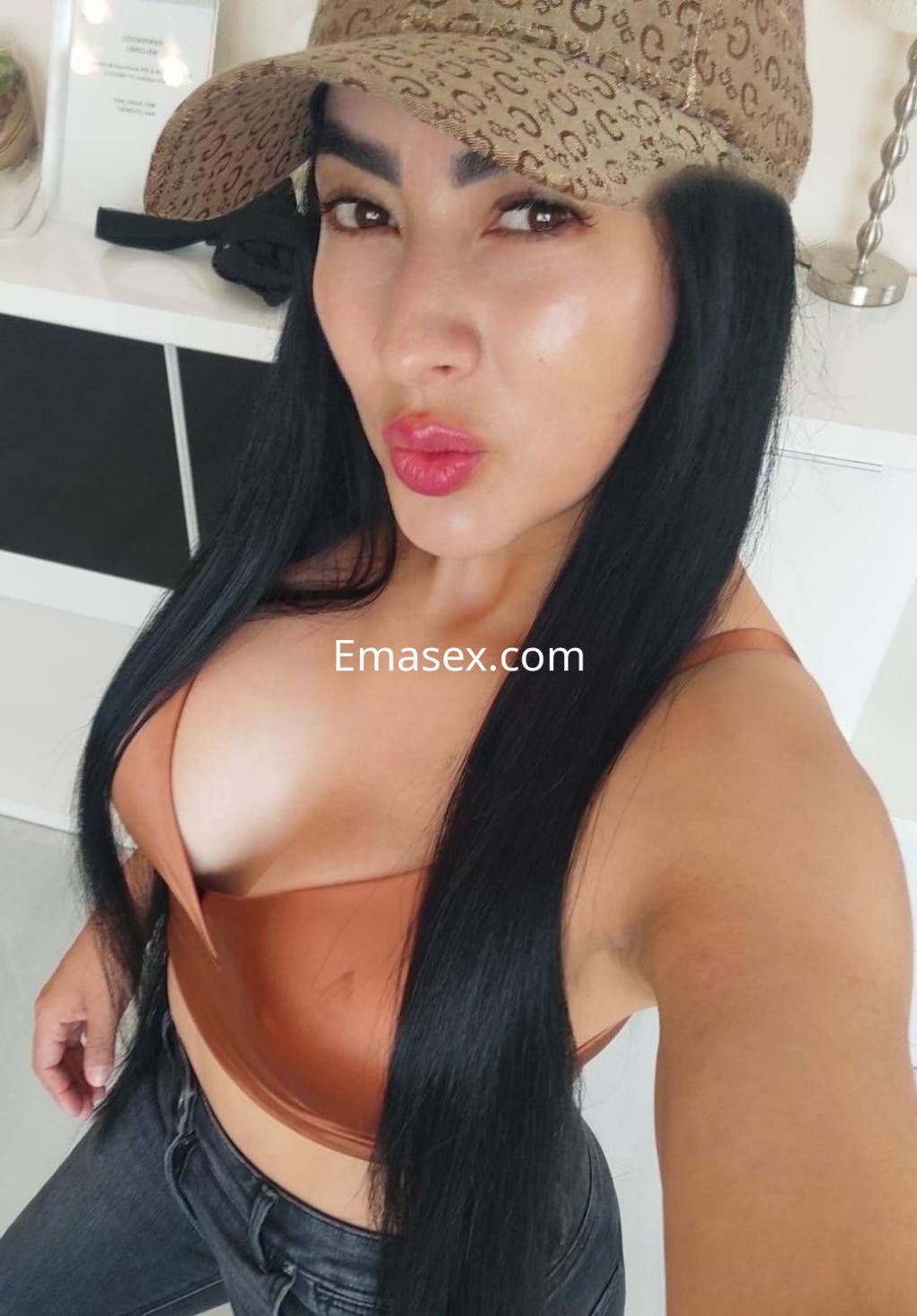 Escort en Madrid con cabello largo y lacio, luciendo un top marrón y jeans, posando con gorra.