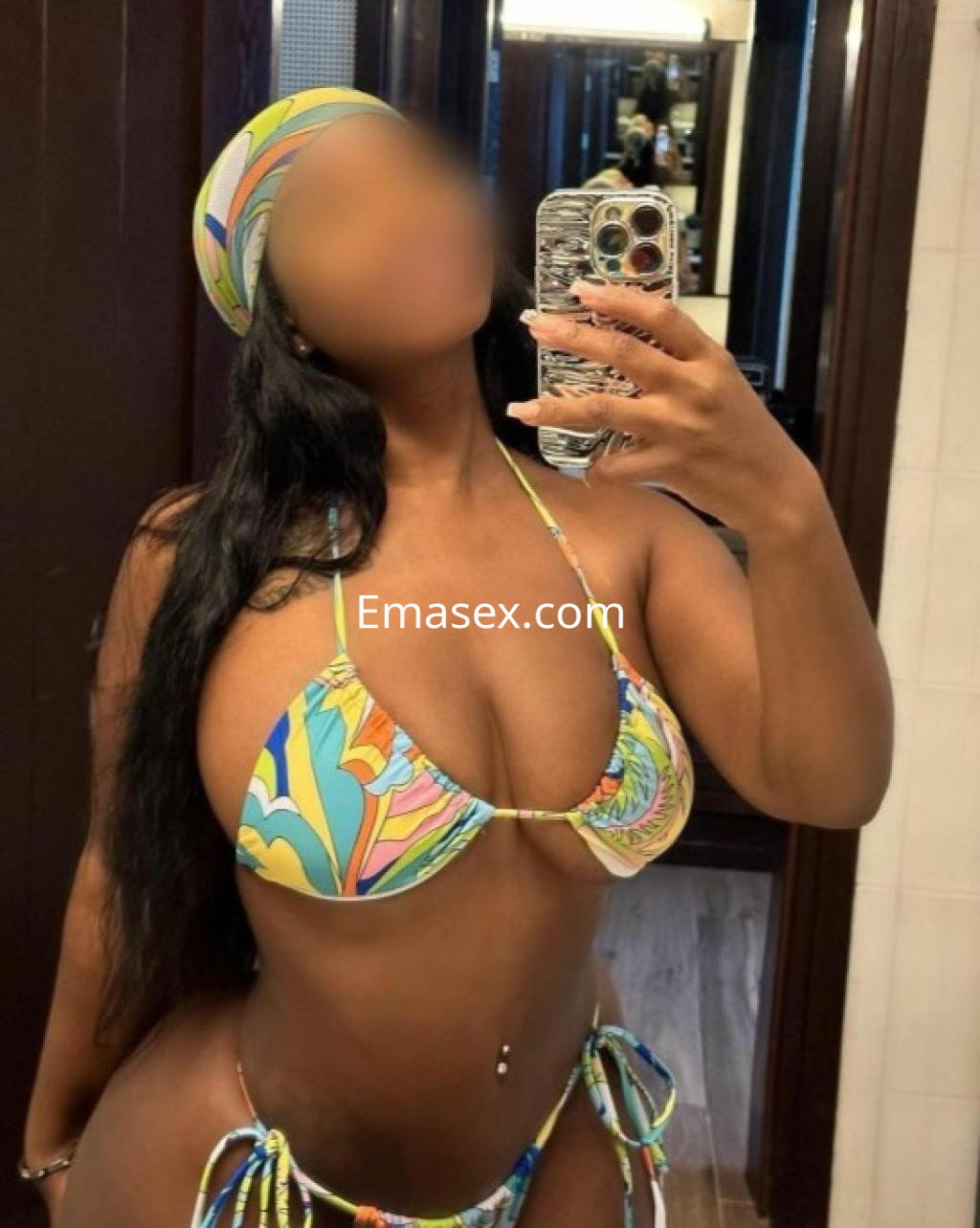 La escort en Badajoz lleva un bikini colorido con estampado floral y se toma una selfie en un espejo.