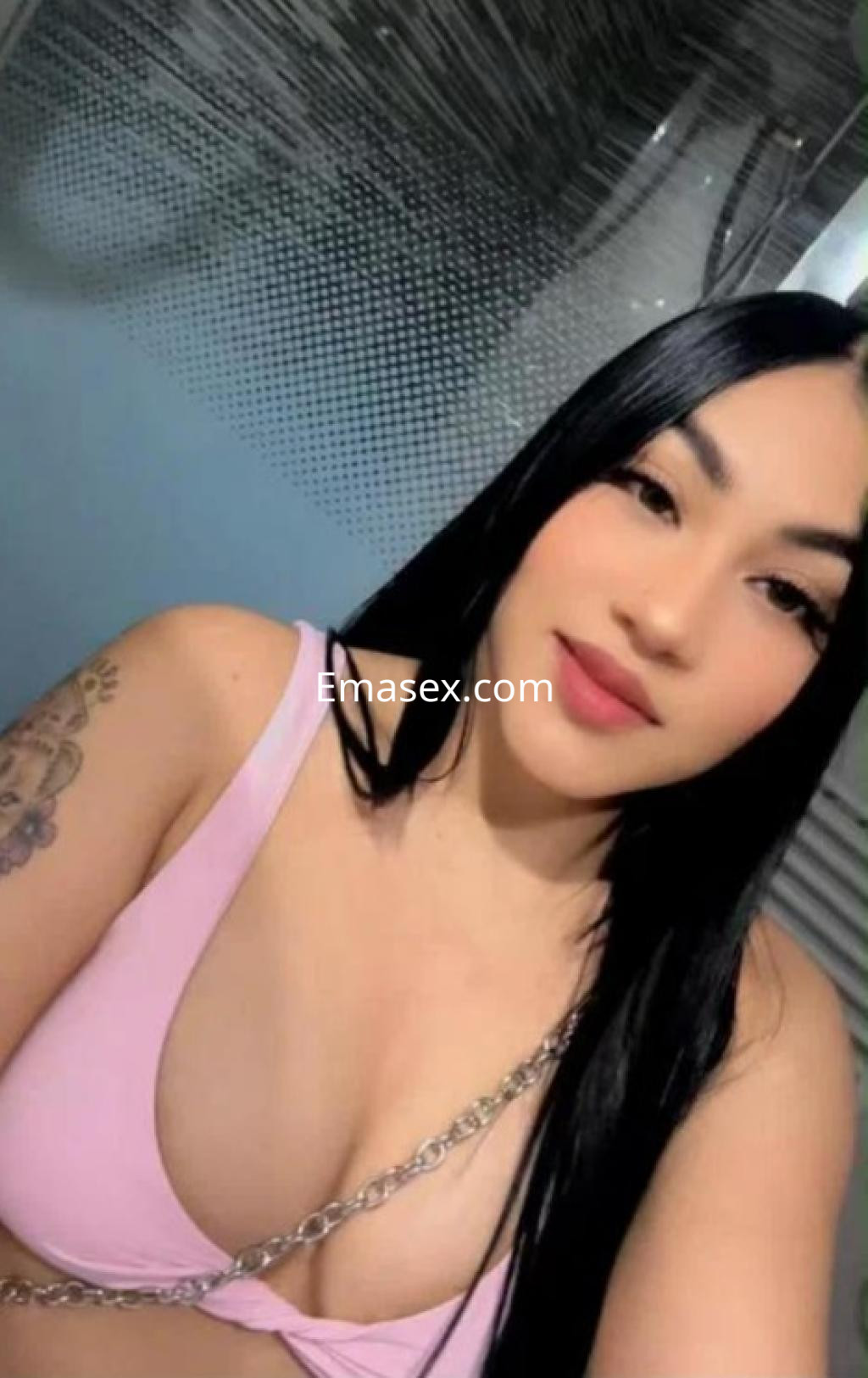 Escort en Valencia con cabello largo y lacio, vistiendo un top rosa, posa sonriente frente a un fondo suave.
