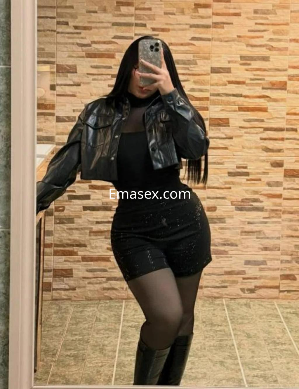 Escort en Burgos con chaqueta de cuero negro, top ajustado y pantalones cortos brillantes en un entorno moderno.