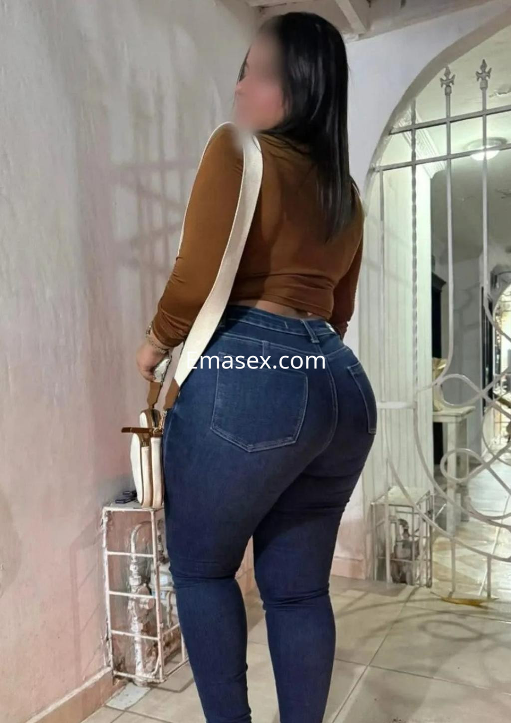 Puta de cabello largo y oscuro, viste un suéter marrón ajustado y jeans, posando de espaldas en Toledo.