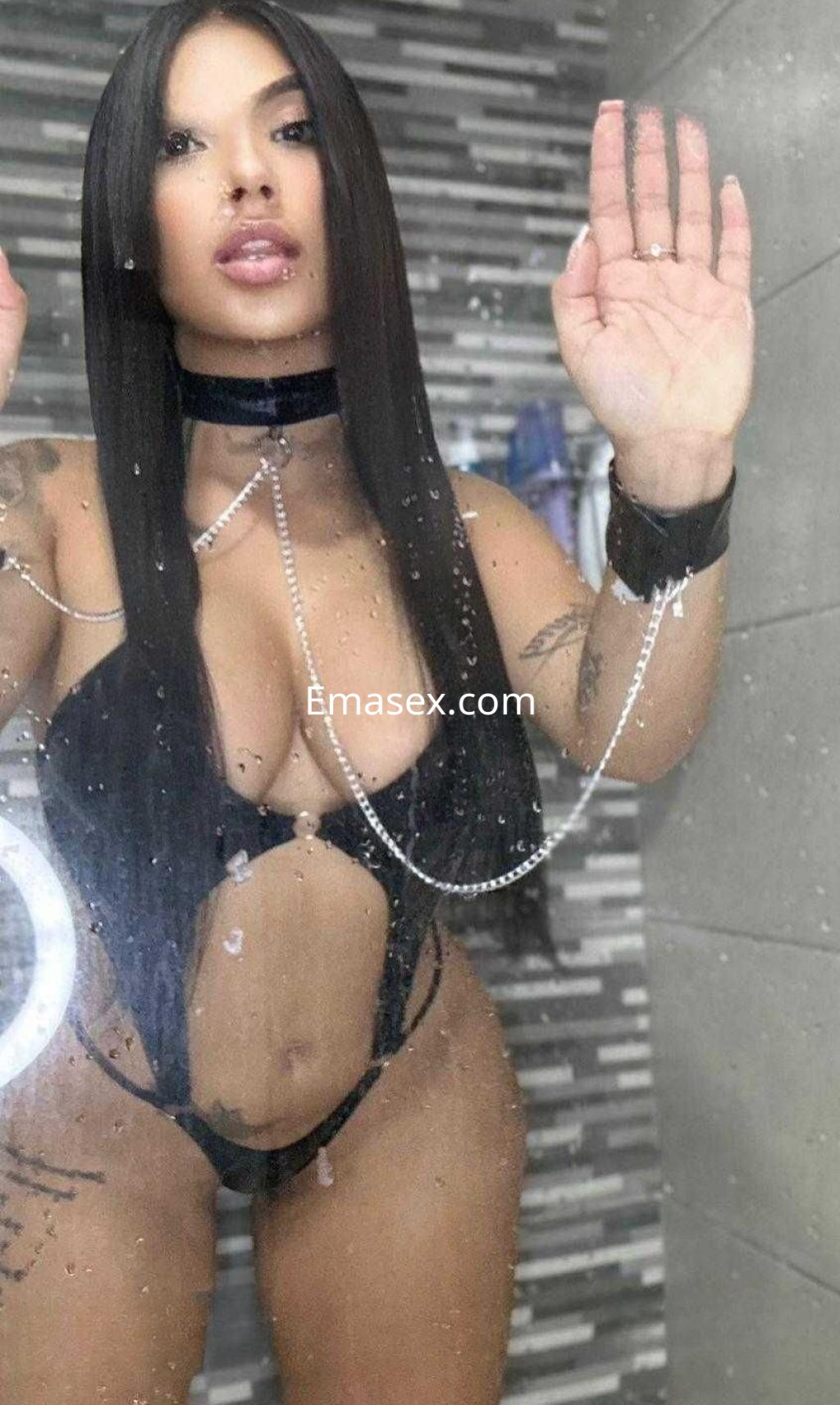 La escort en Cádiz posa frente al espejo con un atrevido conjunto negro, mostrando su figura y tatuajes.